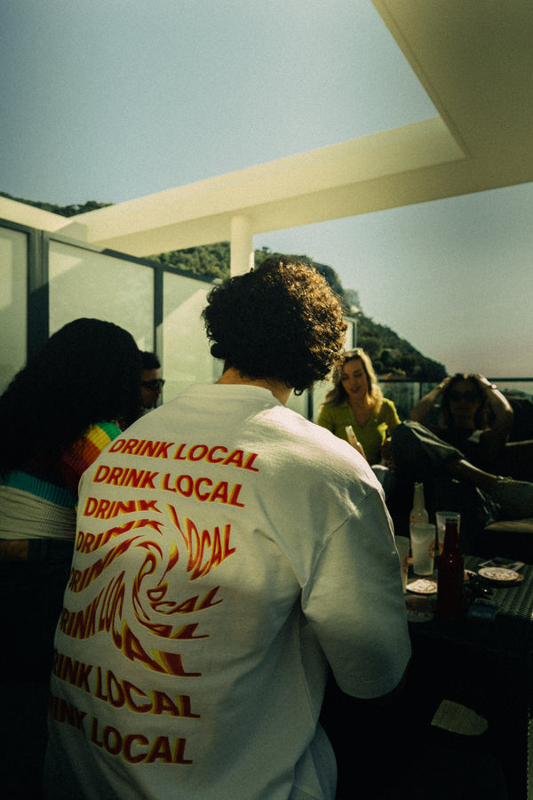 Un homme qui porte le t-shirt Monte Carlo Beer "Drink Local" en blanc de dos avec avec ses amis