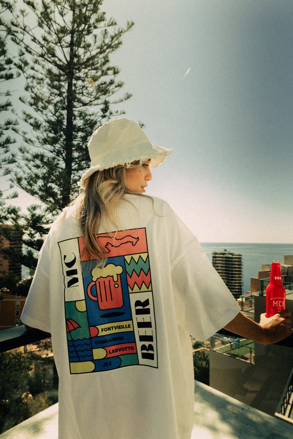 Une femme portant le t-shirt Monte Carlo Beer "starter plaque avec une vue sur la mer et Monaco et une bière ambrée à la main.