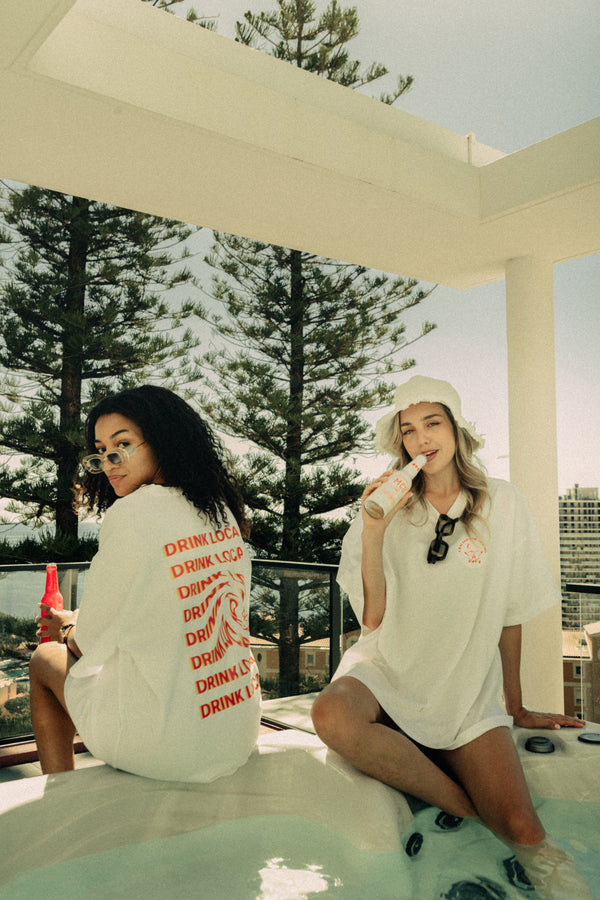 Deux filles dans un jaccuzzi portant le t-shirt Monte Carlo Beer "Drink Local" en blanc tenant une bière blonde et ambrée MCB.