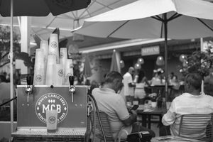 En premier plan une tireuse à bière à deux becs brandé MCB avec des eco cup MCB empilé et posé dessus. En arrière plan un restaurant au bord de mer de Monaco.