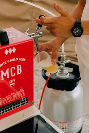 Une main d'homme en train de servir de la bière artisanale Monte Carlo Beer dans un eco-cup à l'aide de la tireuse et fût MCB.