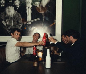 Plusieurs personnes assissent sur une table de bar, trinquant avec des bières blondes et ambrée Monte Carlo Beer 