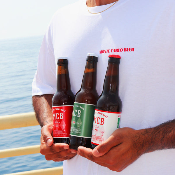 Personne portant un t-shirt Monte Carlo Beer, tenant dans ses mains les trois bières de la marque : IPA, ambrée et blonde.